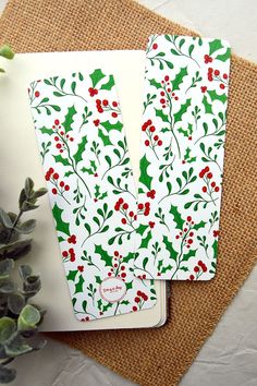 two notebooks with holly and berries on them sitting next to a potted plant