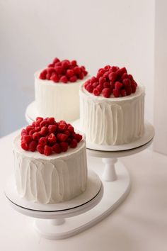 three cakes with white frosting and raspberries on top, one is red