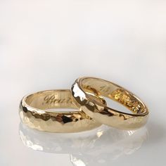 two gold wedding rings sitting side by side on a white surface with reflections in the background