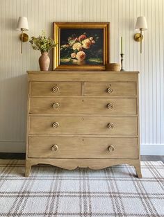 a dresser with flowers on top and a painting above it