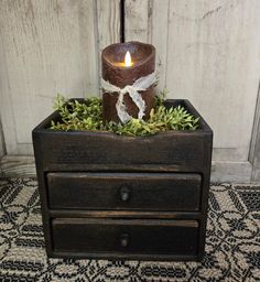 a candle that is sitting on top of a box with some plants in front of it