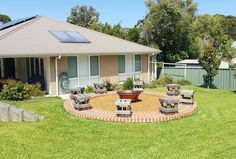 an outdoor patio with chairs and a fire pit in the middle, surrounded by grass