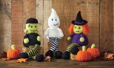 three crocheted halloween dolls sitting next to each other on a wooden surface with leaves and pumpkins