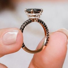 a person holding an engagement ring with black and white diamonds on it's side