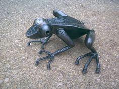 a metal frog sitting on the ground with its legs spread out and eyes wide open