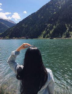 a woman standing on top of a lake holding her hand up to the sky with mountains in the background