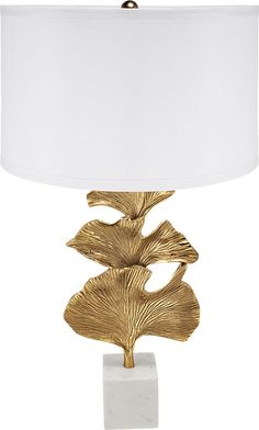 a gold leaf lamp on a white base with a white lampshade behind it