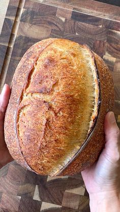 a person holding a loaf of bread on top of a cutting board