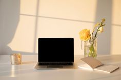 an open laptop computer sitting on top of a table next to a vase with yellow flowers