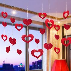 red hearts hanging from strings in front of a window with a lamp on the side