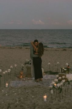 a couple embracing on the beach with candles in front of them and flowers all around