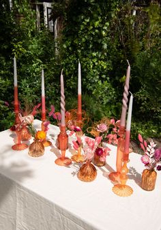 there are many candles on the table with flowers in vases next to each other