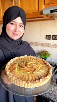 a woman in hijab holding a pie on a glass platter and smiling at the camera