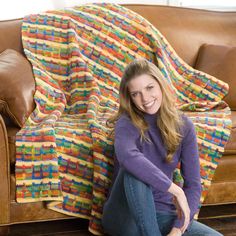 a woman sitting on the floor in front of a couch with a crocheted blanket