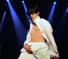 a shirtless man is on stage in front of spotlights and blue lights with his pants rolled up