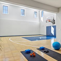 an indoor basketball court with blue and orange balls on the floor in front of it