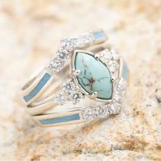 a turquoise stone and diamond ring sitting on top of a rock