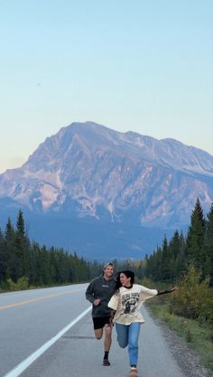 two people running down the road in front of a mountain