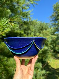 a hand holding a blue glass bowl with beads on the outside and trees in the background