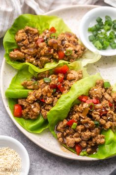 lettuce wraps filled with meat and vegetables on a plate next to small bowls