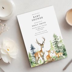 a baby shower card with deer and pine trees on it next to a cup of tea