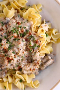 a white bowl filled with pasta covered in gravy and garnished with parsley