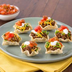 small appetizers are arranged on a plate with salsa and sour cream in the background