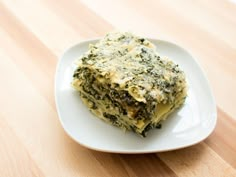 a white plate topped with lasagna covered in cheese and spinach on top of a wooden table