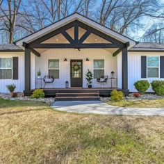 a white house with black trim on the front porch and covered in grass, surrounded by trees