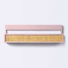 a pink and gold wall hanging on the side of a white wall next to a wooden shelf