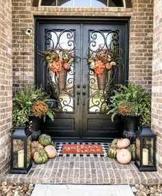 front door decorated with pumpkins and potted plants on brick walkway next to black double doors