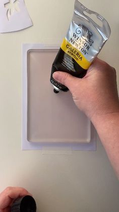 a hand holding a tube of cream on top of a white surface next to a plastic container