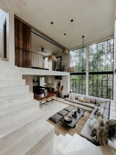 a living room filled with lots of furniture next to tall windows on top of a stair case