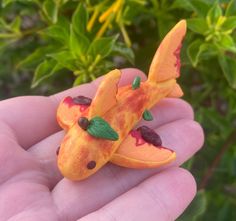 a hand holding a tiny orange toy fish in it's left side and green leaves on the other side