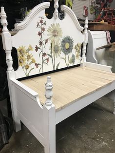 a white bed frame with flowers painted on the top and bottom part, sitting in a shop