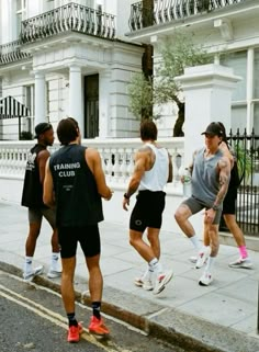 four men are playing basketball on the sidewalk in front of a white building and black iron fence