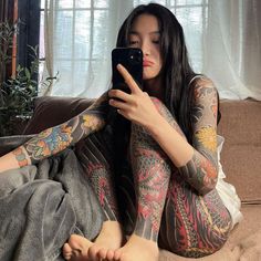 a woman with tattoos on her body is looking at her cell phone while sitting on the couch