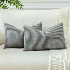 two gray pillows sitting on top of a white couch