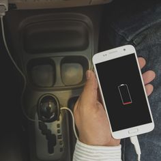 a person holding a cell phone in their hand next to an electronic device with a charger plugged into it