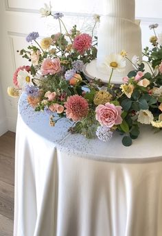 a white wedding cake on top of a table covered in flowers and greenery next to a window