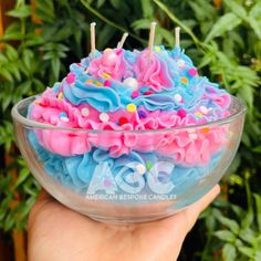 a hand holding a glass bowl filled with blue, pink and white frosted cake