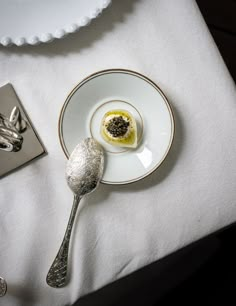 a white plate topped with an egg on top of a table next to silver spoons