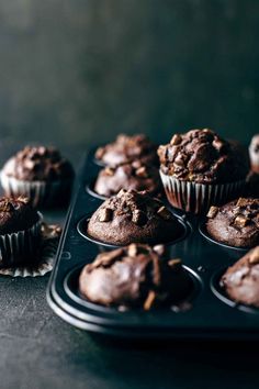 chocolate muffins sitting on top of a black tray next to cupcake tins