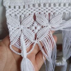 a hand is holding a piece of white crocheted fabric with tassels