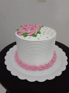 a white and pink cake with flowers on top sitting on a black table in front of a wall