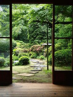 an open door leading into a lush green garden with stepping stones on the ground and trees in the background