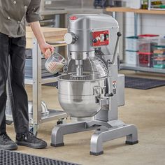 a man is pouring something into a large metal mixing bowl while standing in front of an industrial mixer