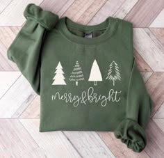 a green sweatshirt that says merry and bright with white trees on the front, sitting on a wood floor