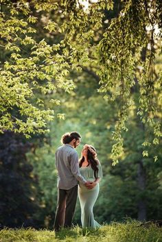 a pregnant couple standing under a tree in the woods