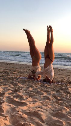 two women doing handstands on the beach at sunset with their feet in the air